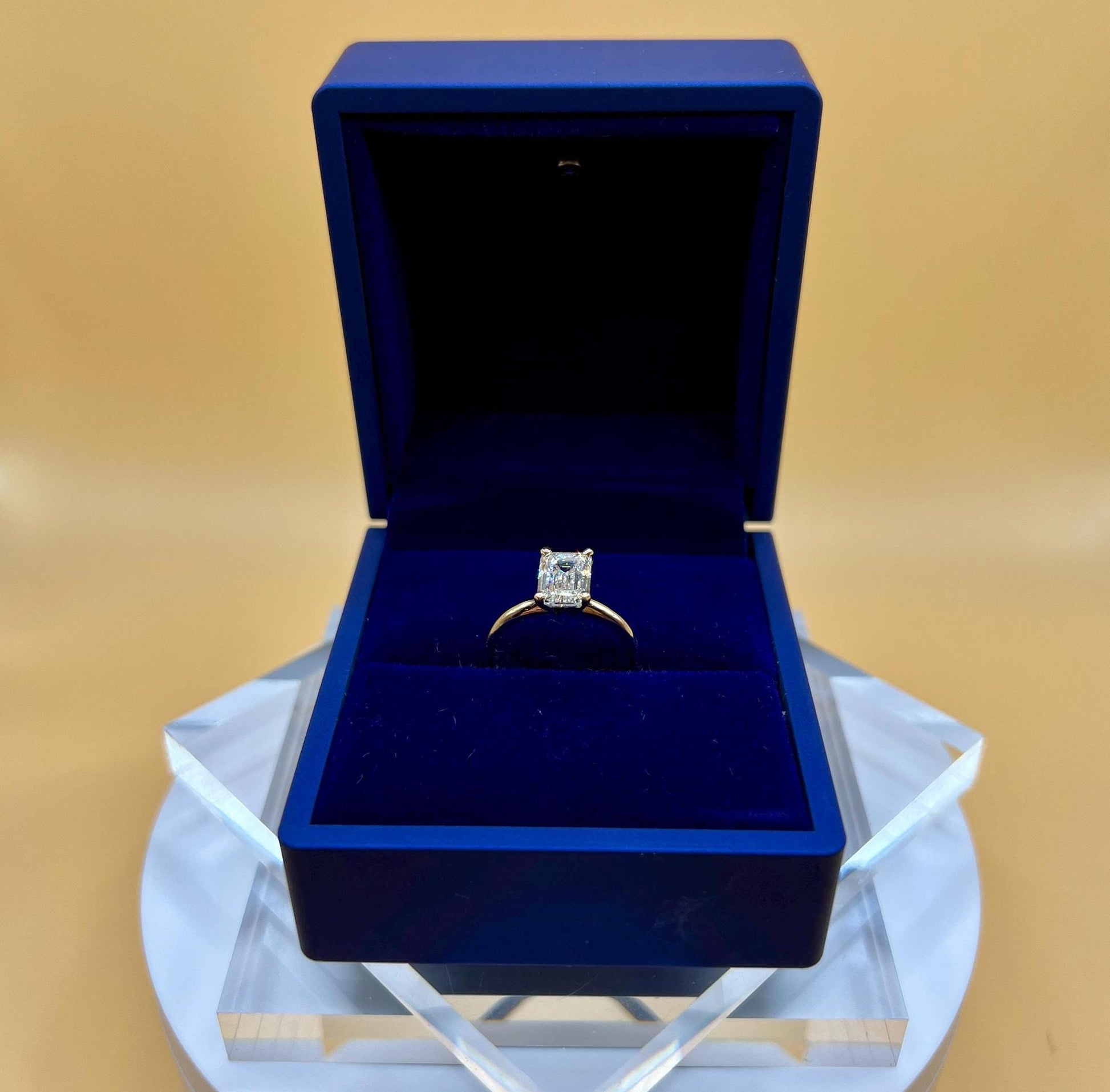 Close-up of 6 carat emerald cut lab grown diamond solitaire engagement ring in solid 14K gold, photographed on a soft background.