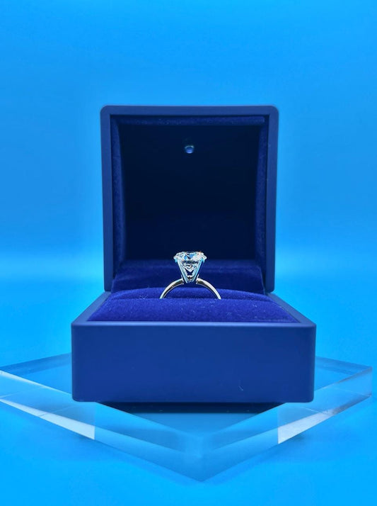Close-up of a 6 carat round lab grown diamond engagement ring set in 14K gold solitaire setting, shown on a neutral background.