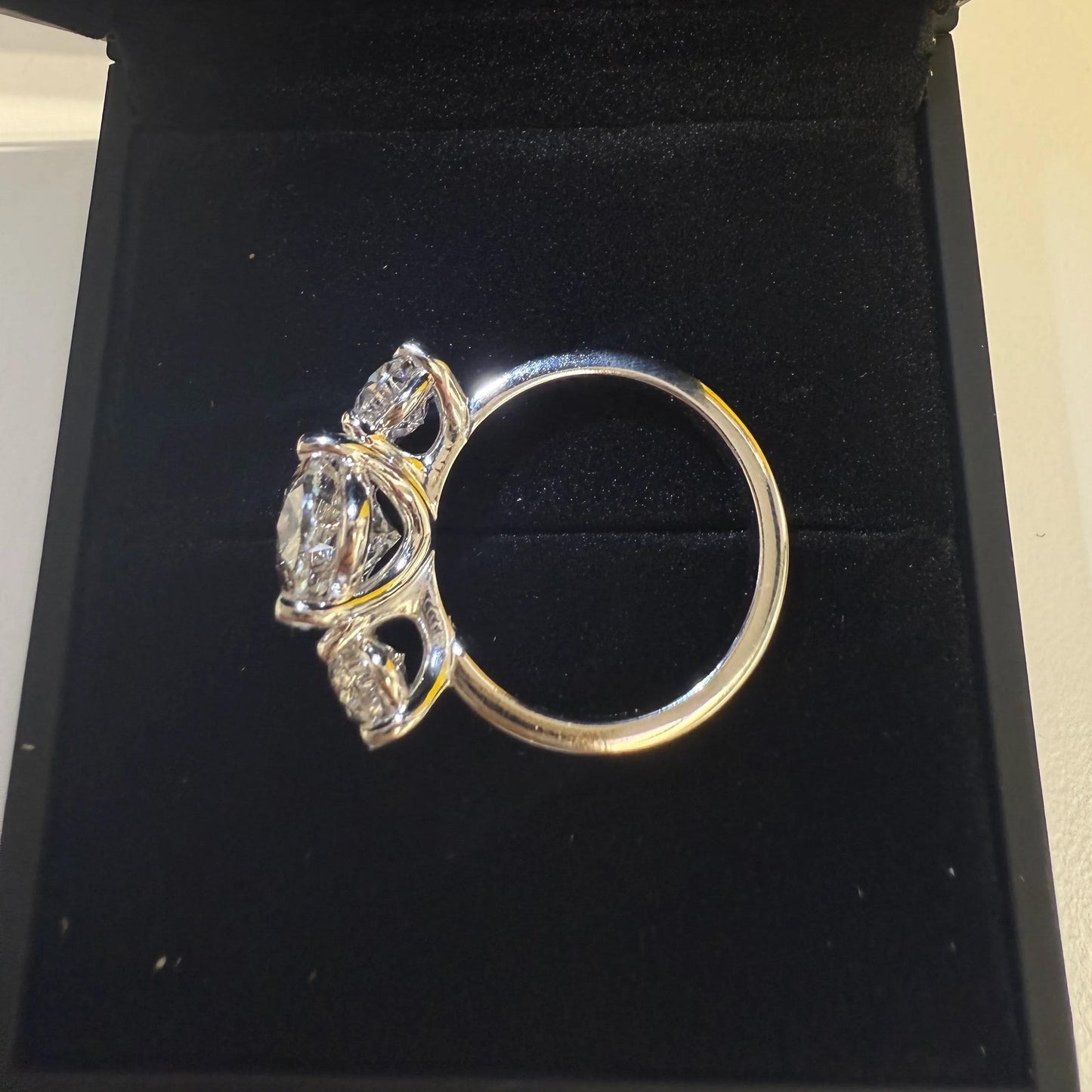A silver ring with a large central diamond surrounded by smaller diamonds, displayed in a black jewelry box.