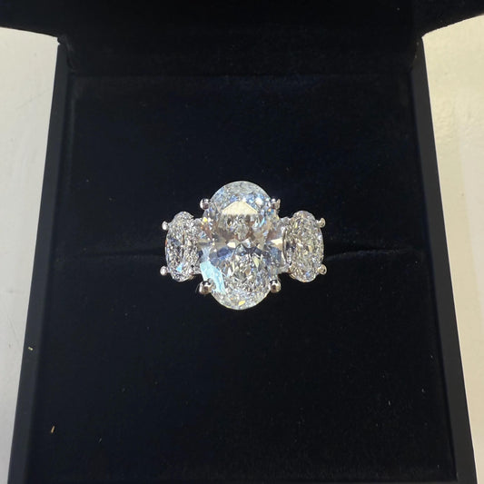 A large, sparkling diamond ring is displayed in a black jewelry box.