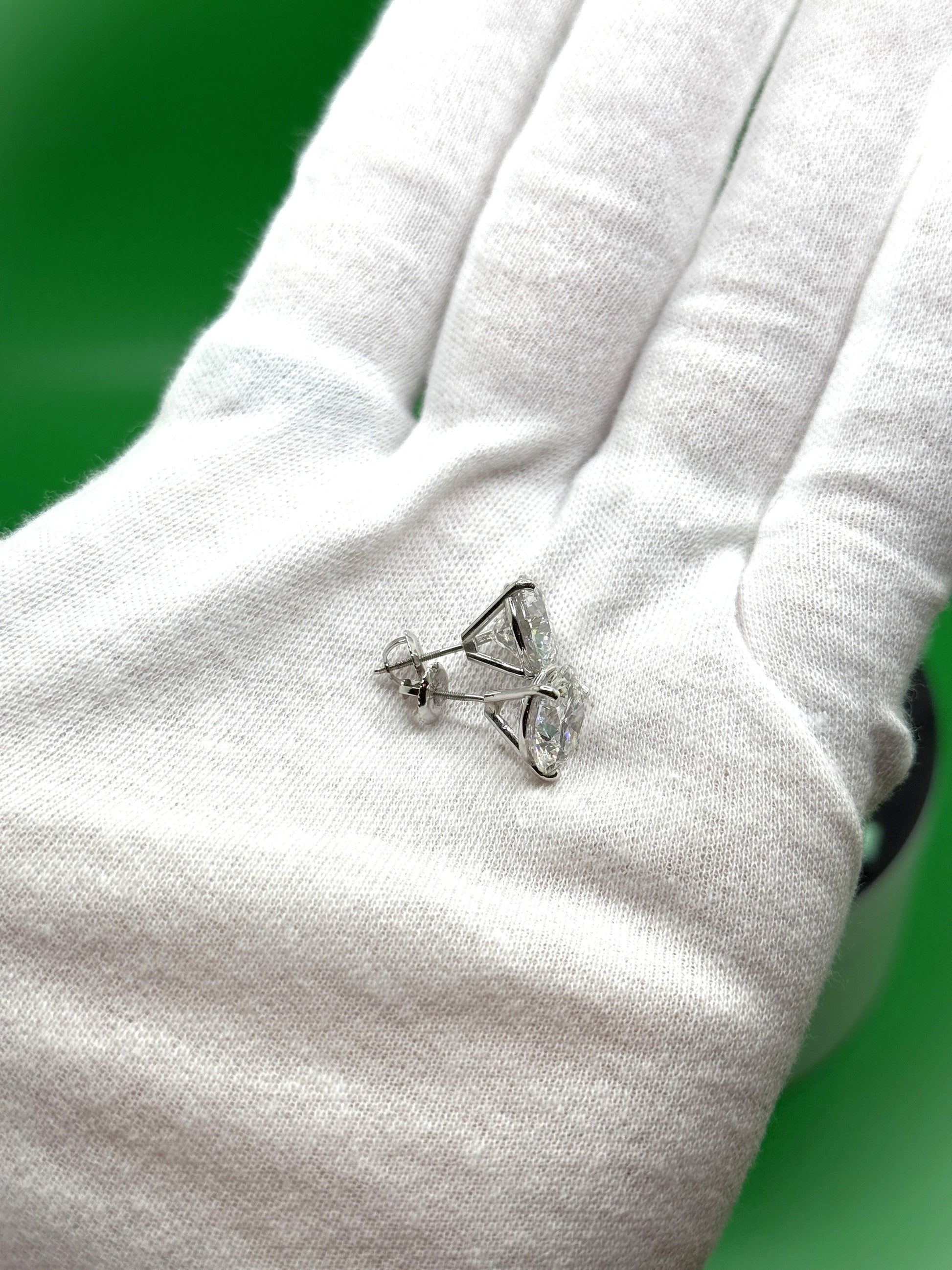 A close-up image of a person's hand wearing a white glove, holding a small silver earring with a clear gemstone.