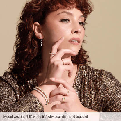 A woman with curly red hair wearing a sparkling gold sequin dress and a bracelet with pear diamonds, posing with her hand on her chin.