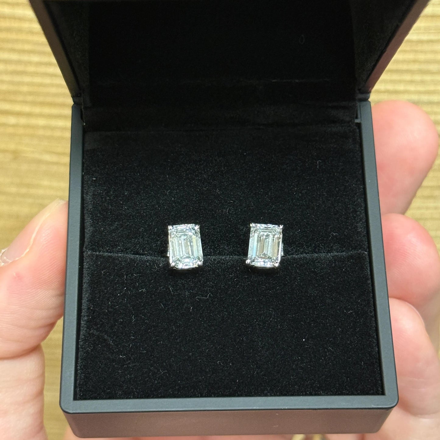 A hand holding a black jewelry box containing two diamond earrings.