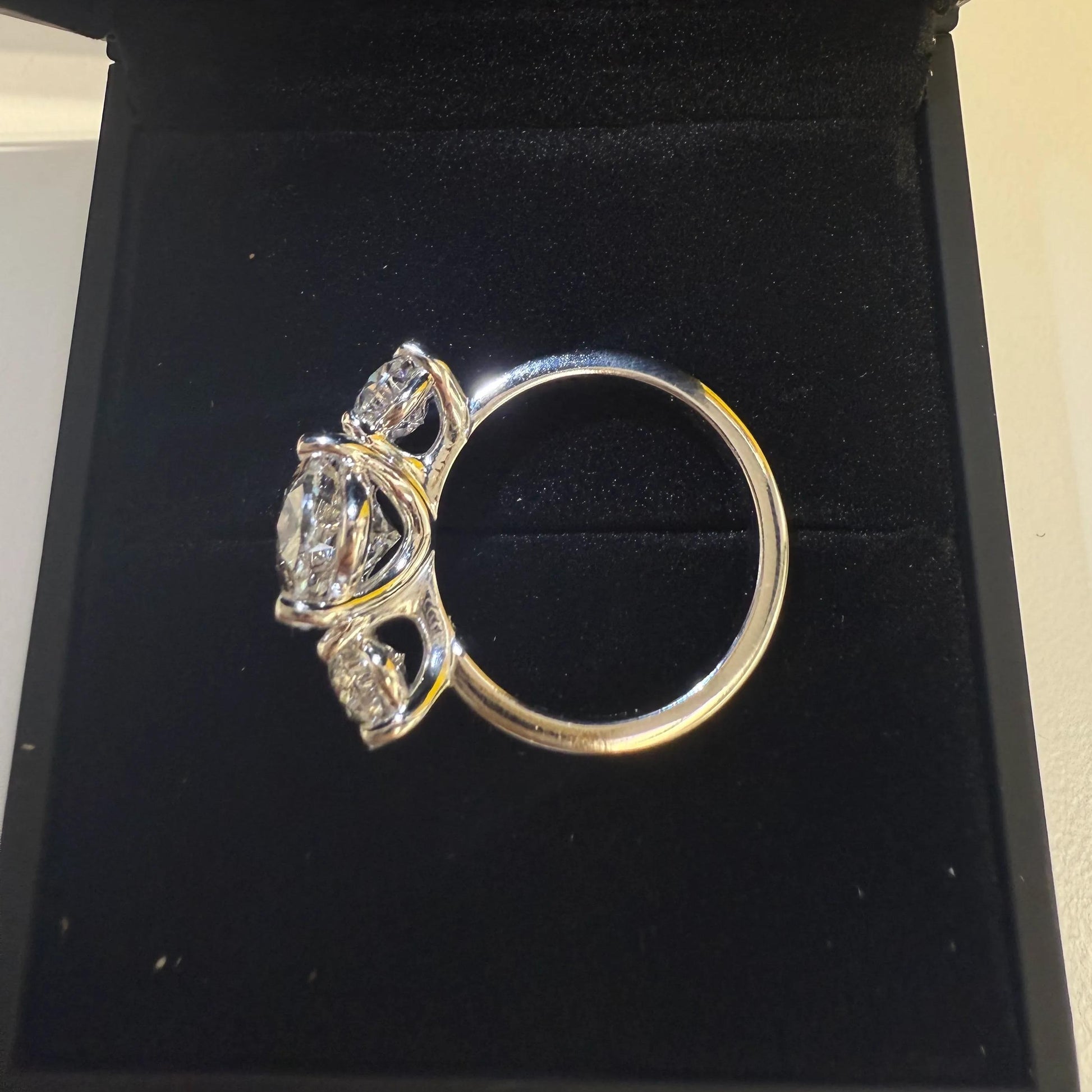 A silver ring with a large central diamond surrounded by smaller diamonds, displayed in a black jewelry box.