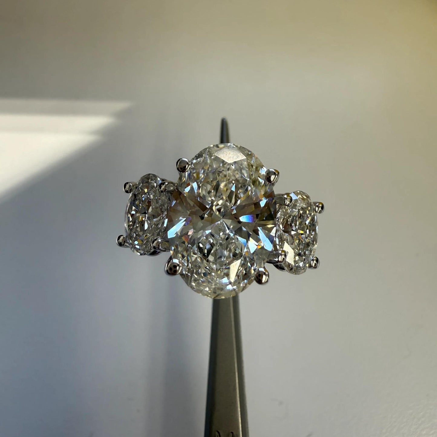 A close-up image of a diamond ring with a large central diamond surrounded by smaller diamonds, displayed on a metal object.