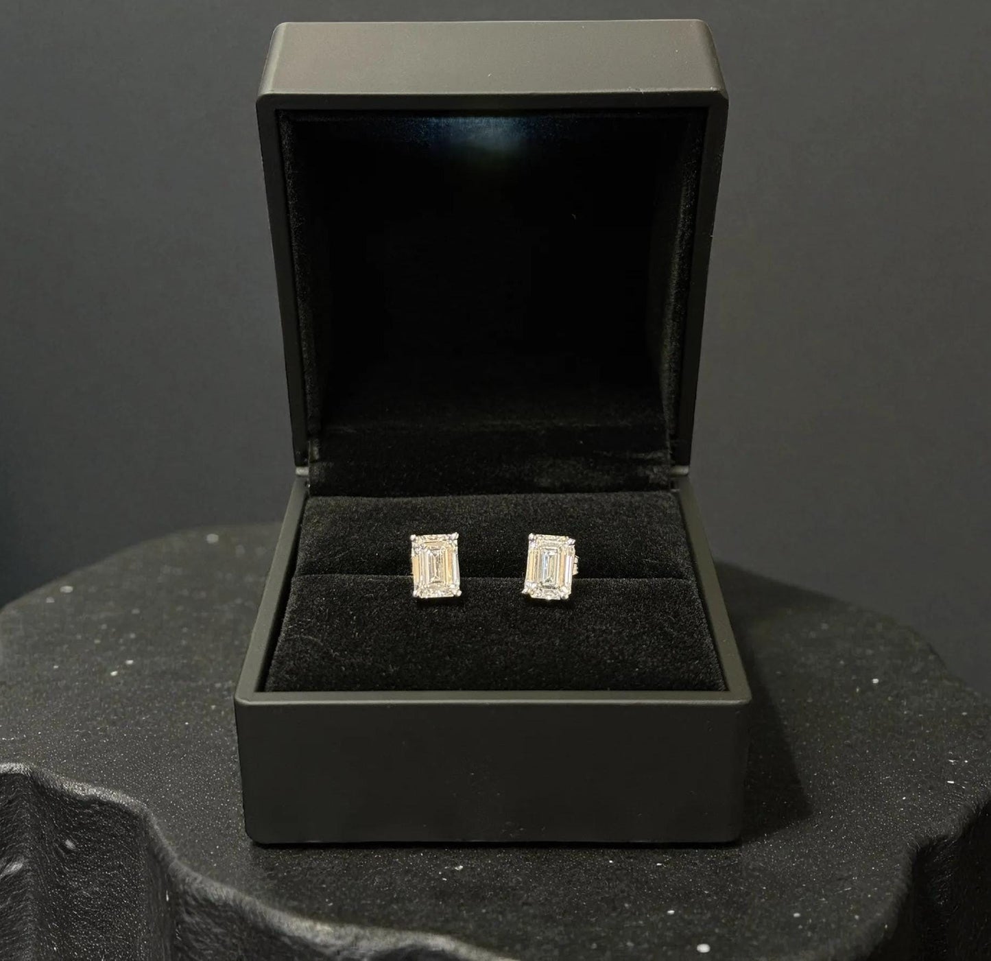 A pair of diamond earrings is displayed in a black jewelry box on a black surface.