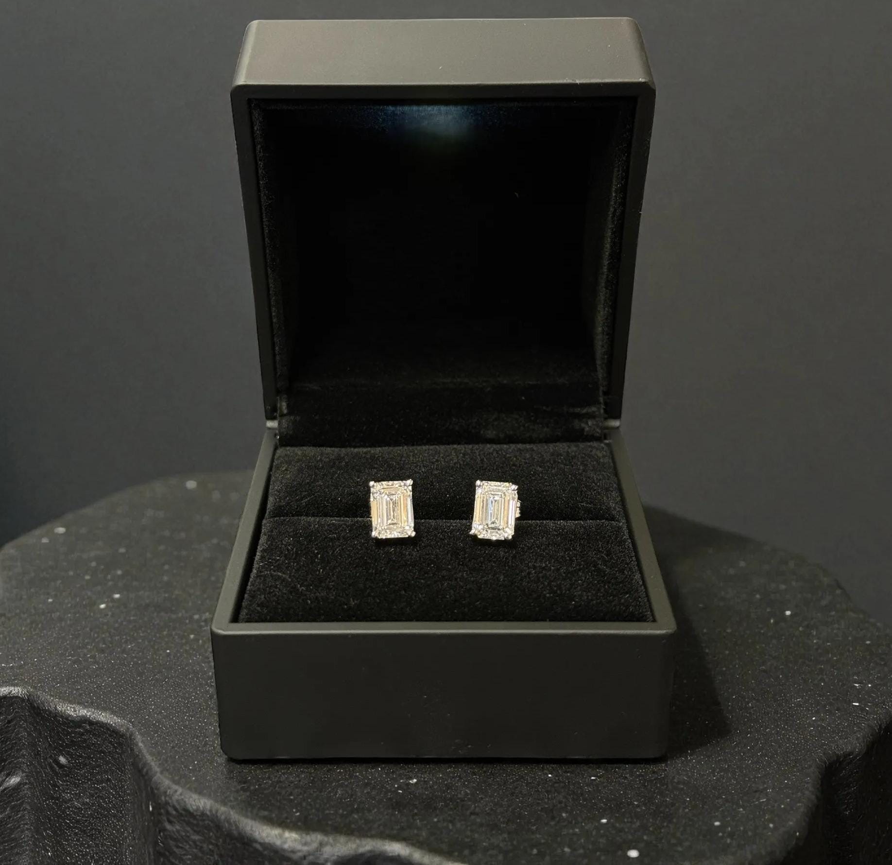 A pair of diamond earrings is displayed in a black jewelry box on a black surface.