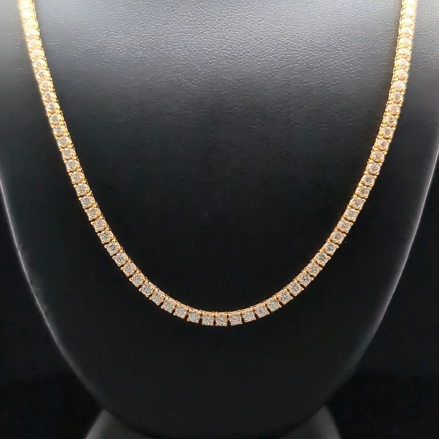 A gold necklace with small diamonds displayed on a black mannequin.