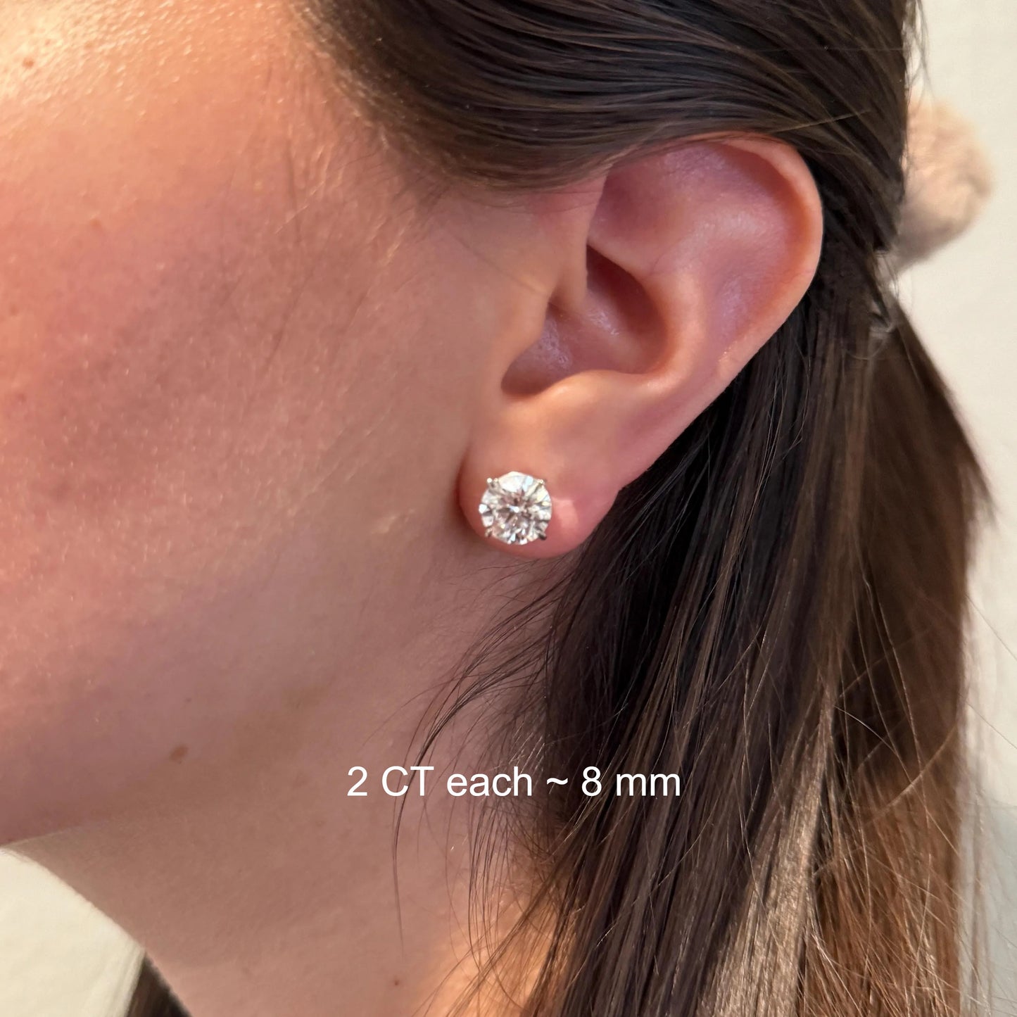 A close-up of a person's ear with a large, clear diamond earring.
