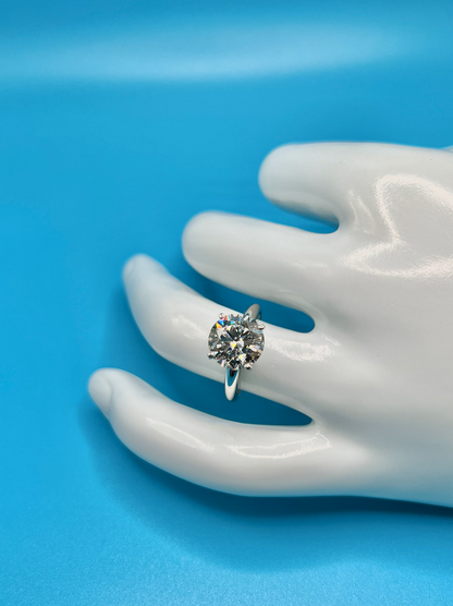 A close-up image of a white mannequin hand wearing a diamond ring against a blue background.