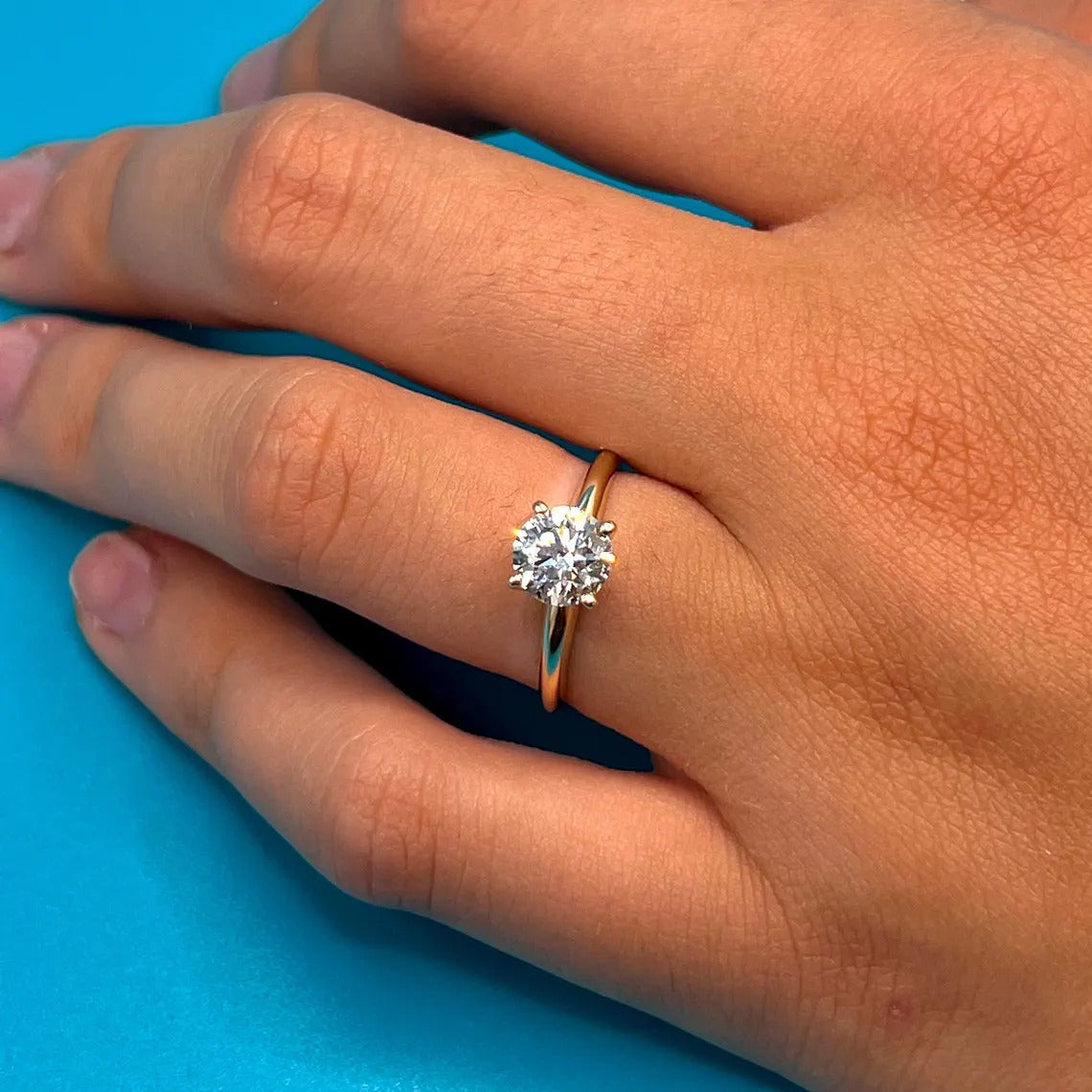 A close-up of a person's hand wearing a gold ring with a large diamond center stone.