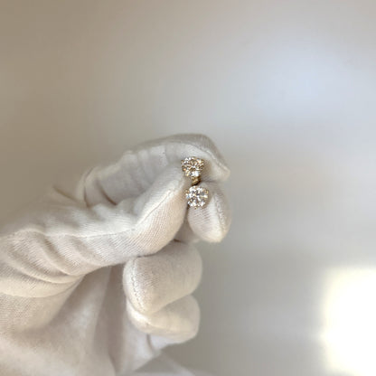 A hand wearing a white glove holds a pair of diamond earrings against a blurred background.