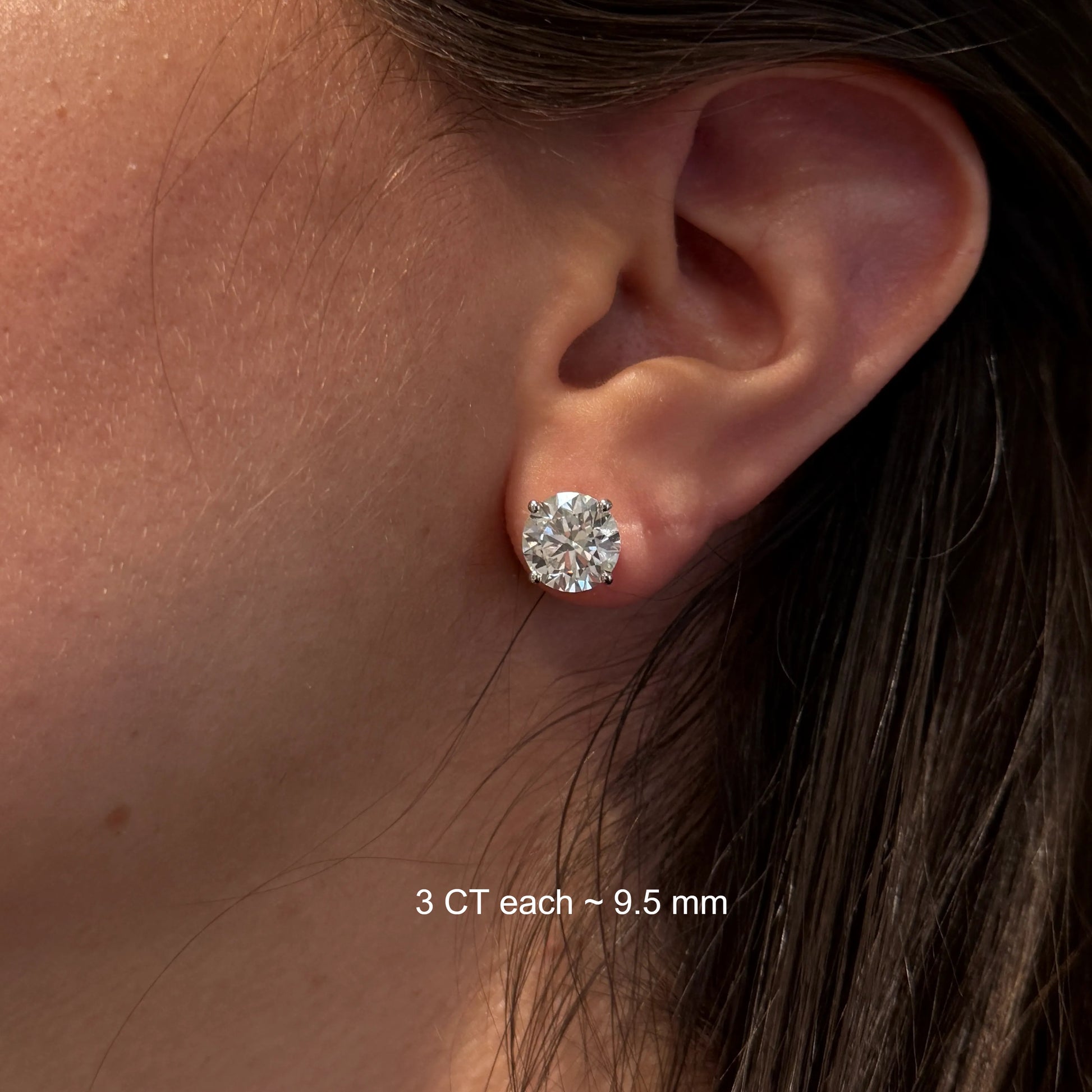 A close-up of a person's ear with a large, clear diamond earring in the earlobe.